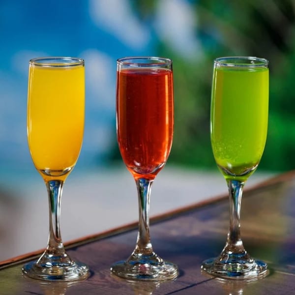 Three colorful Caribbean drinks in champagne flutes: yellow, red, and green, against a blue and green background.