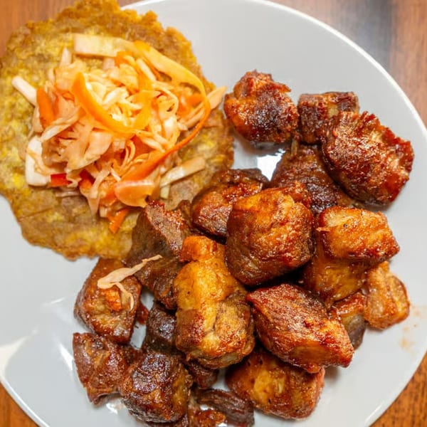 Fried pork chunks with a side of plantain and pickled cabbage on a white plate.