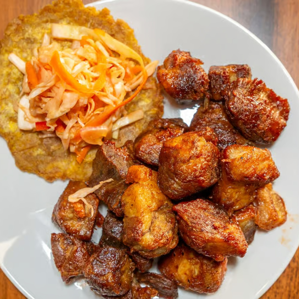 Fried pork chunks with a side of plantain and pickled cabbage on a white plate.
