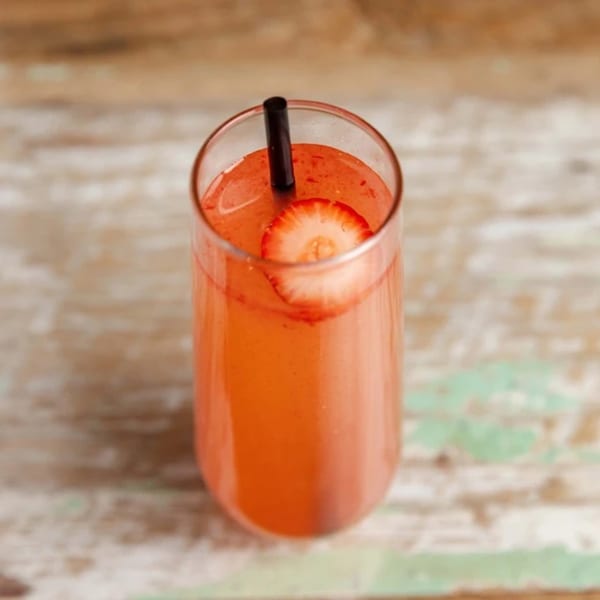 A vibrant pink Caribbean cocktail with a strawberry slice and black straw on a rustic wooden table.