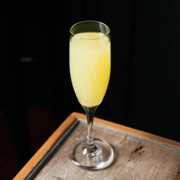 A tall, slender glass filled with a vibrant yellow Caribbean cocktail sits on a wooden surface.