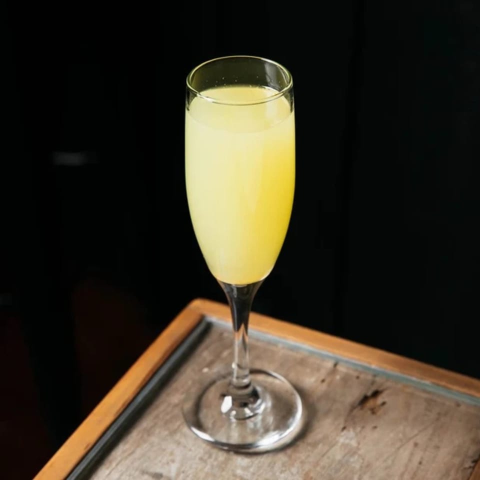 A tall, slender glass filled with a vibrant yellow Caribbean cocktail sits on a wooden surface.