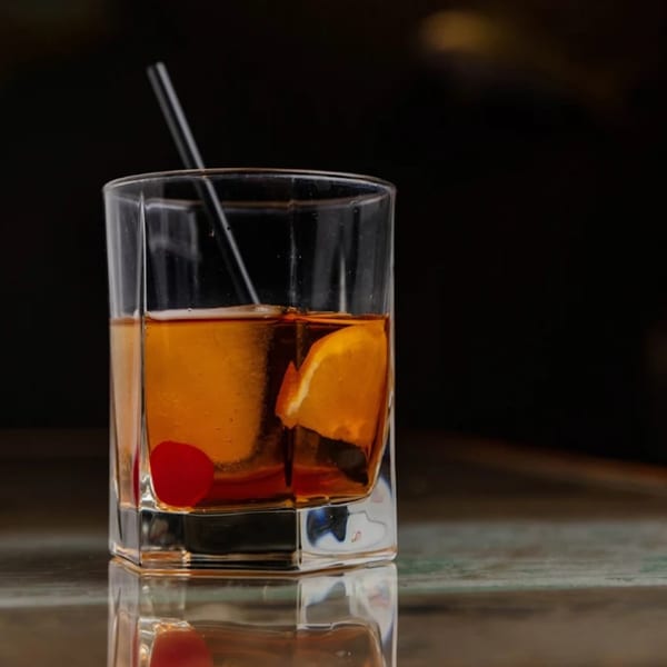 A Bullfish Bistro cocktail with a cherry, orange slice, and straw in a glass.