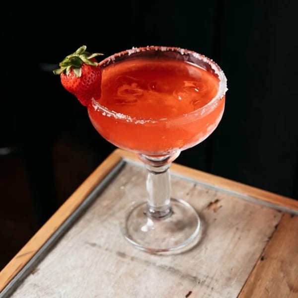 A vibrant red strawberry margarita with a salted rim and a fresh strawberry garnish.