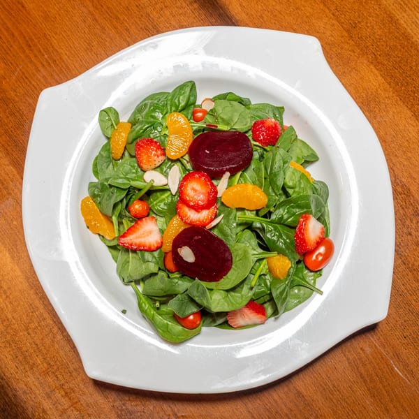 A vibrant spinach salad with strawberries, orange segments, beets, and cherry tomatoes on a white plate.