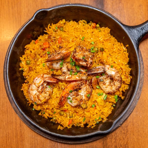 Caribbean shrimp and yellow rice with vegetables in a black skillet on a wooden table.