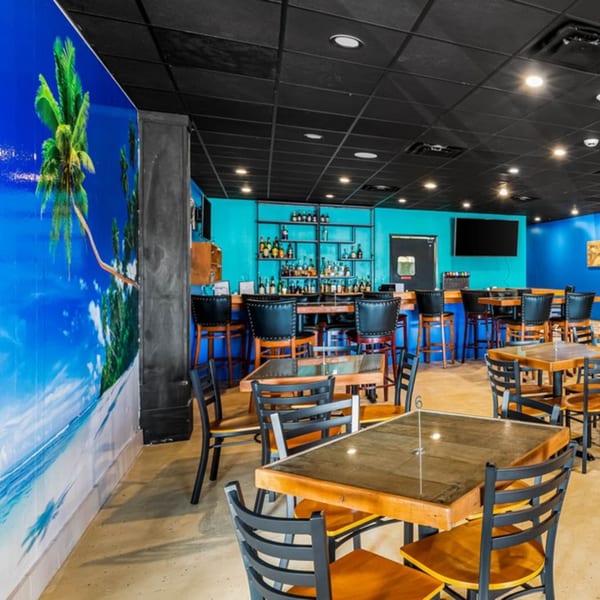 Bullfish Bistro's dining room with a tropical mural, bar, and empty tables and chairs.