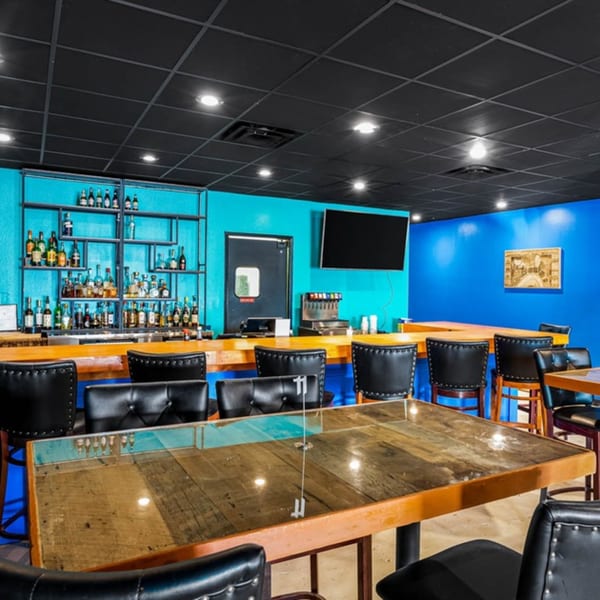 Bullfish Bistro's vibrant bar area with blue walls, a fully stocked bar, and wooden tables with black chairs.