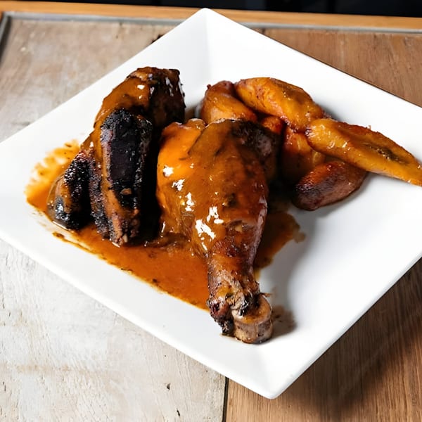 Caribbean jerk chicken with plantains, coated in a rich, savory sauce on a white plate.
