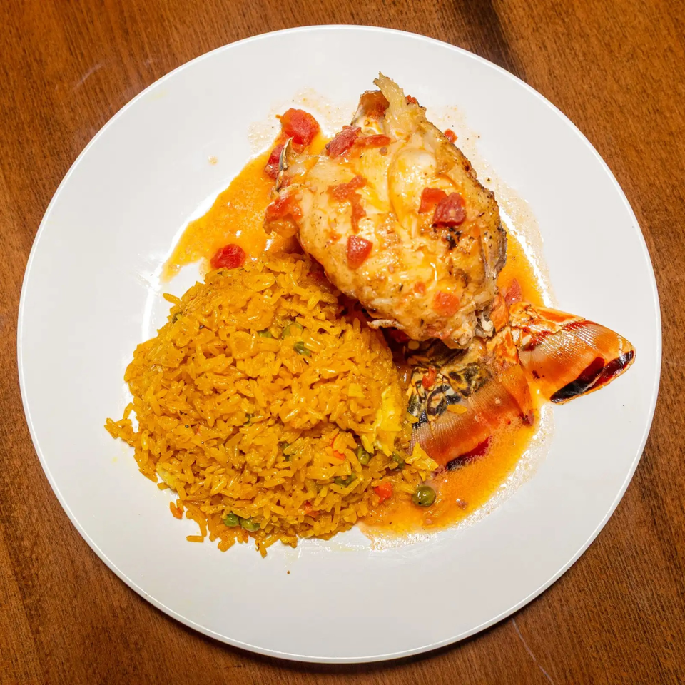 A white plate holds a lobster tail with tomato sauce and a side of yellow rice.